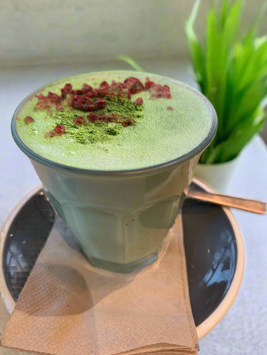 Green matcha latte with toppings in a glass cup on a saucer with a plant in the background.